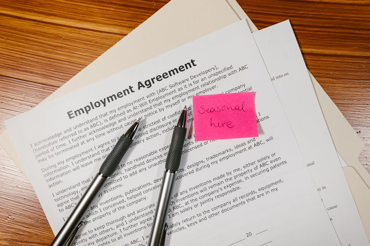 about-us-02 Top view of employment agreement contract with pens and seasonal hire note on wooden desk.